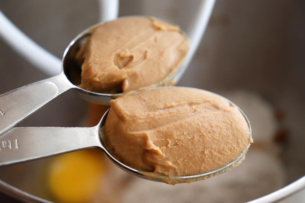 Adding all natural peanut butter to the bowl of an electric mixer